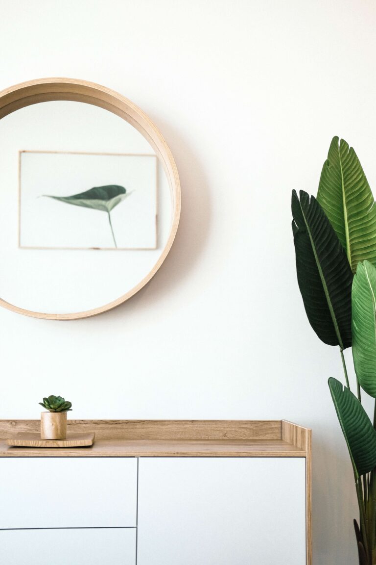 White sideboard below a round mirror, with a large plant to the right